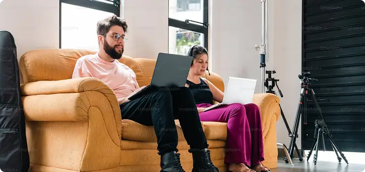 two people sitting on yellow sofa working on laptops